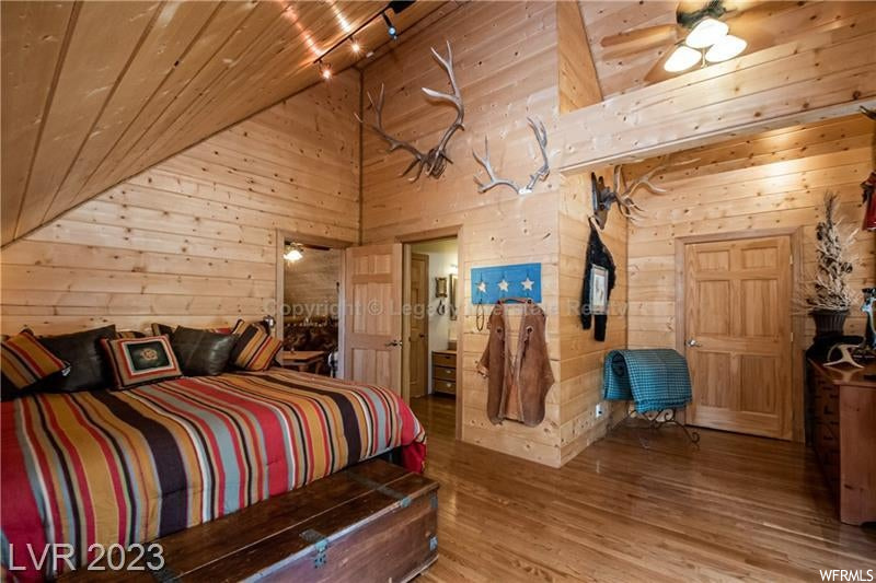Bedroom featuring vaulted ceiling, wooden ceiling, wooden walls, and light hardwood flooring