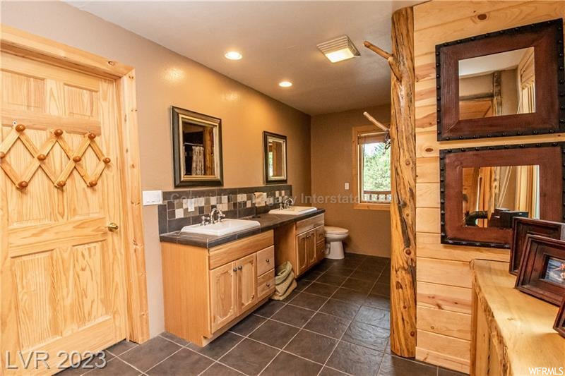 Bathroom with mirror, dual bowl vanity, dark tile flooring, and backsplash