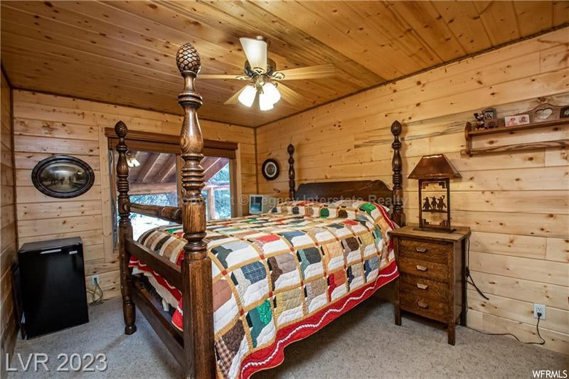 Carpeted bedroom featuring ceiling fan, wooden walls, and wooden ceiling