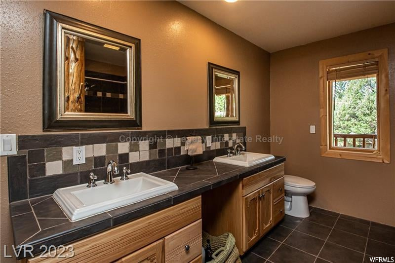 Bathroom featuring mirror, dark tile flooring, backsplash, and dual large bowl vanity