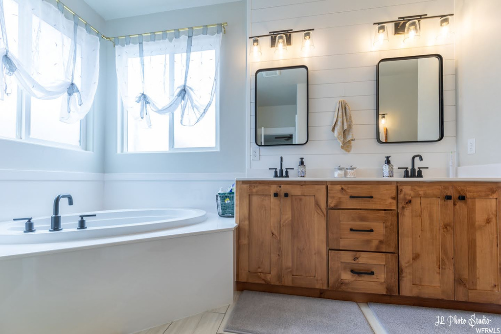 Bathroom with mirror, a bath to relax in, dual large vanity, and plenty of natural light