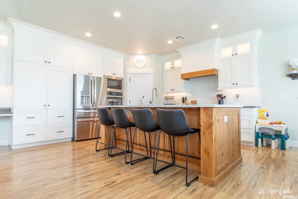 Kitchen with white cabinets, backsplash, appliances with stainless steel finishes, a kitchen island, light parquet floors, and light countertops