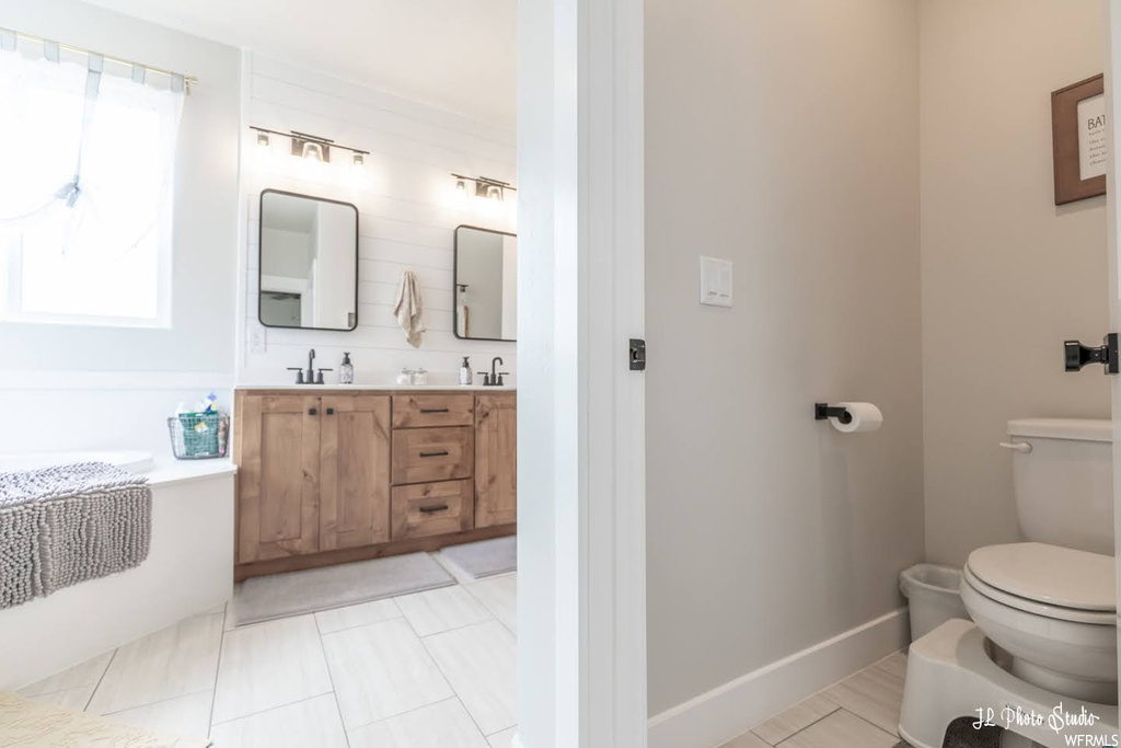 Bathroom with dual vanity, light tile floors, and mirror
