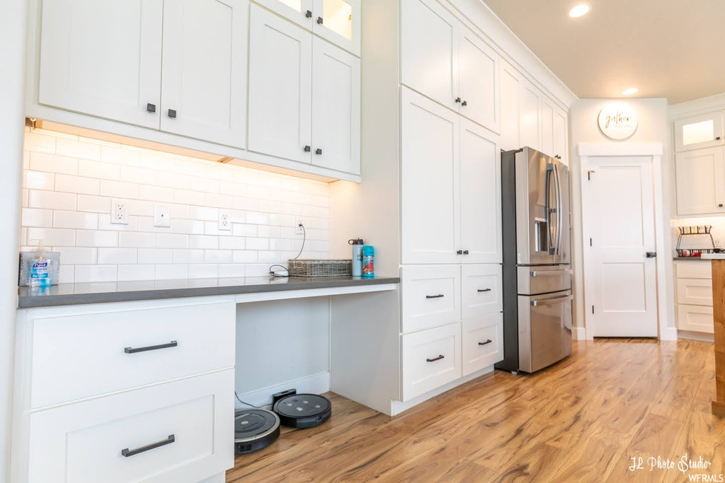 Kitchen with dark countertops, light hardwood flooring, backsplash, white cabinetry, and stainless steel fridge with ice dispenser