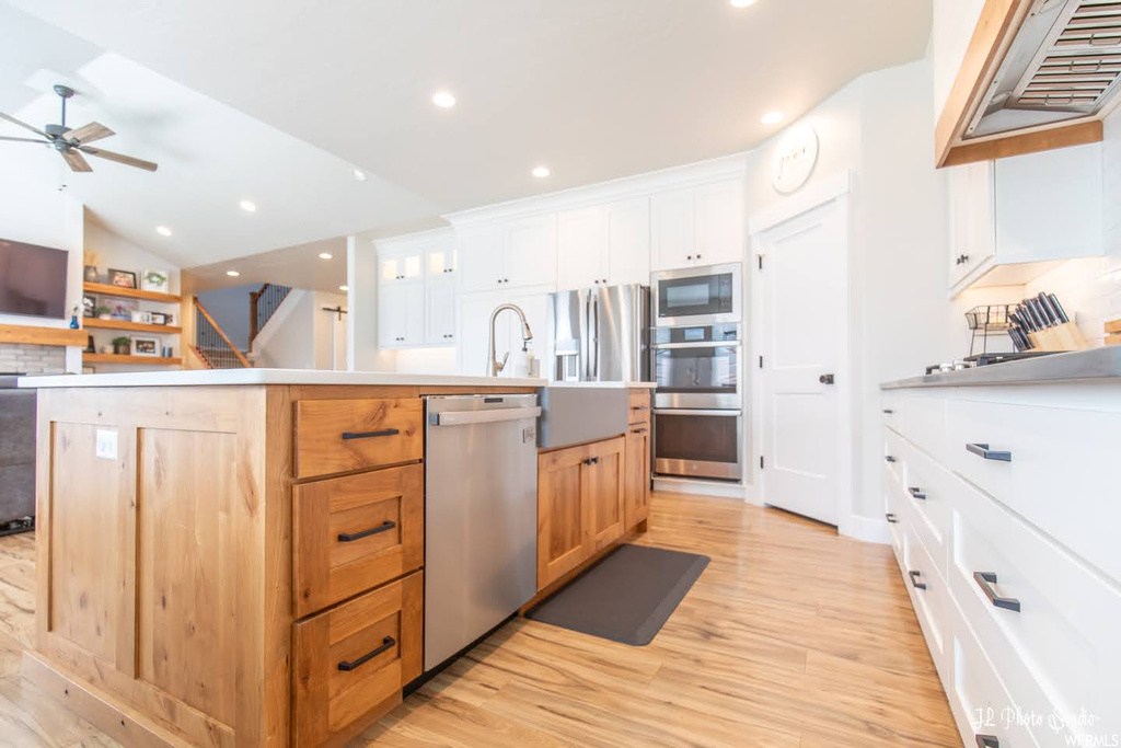 Kitchen featuring white cabinets, light hardwood floors, vaulted ceiling, stainless steel appliances, backsplash, ceiling fan, and light countertops