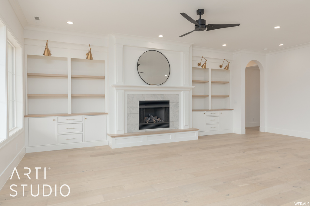 Hardwood floored living room featuring ornamental molding, built in shelves, a fireplace, and ceiling fan