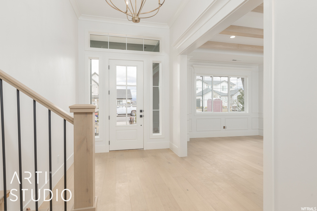 Foyer entrance with ornamental molding, a healthy amount of sunlight, light hardwood floors, and beamed ceiling