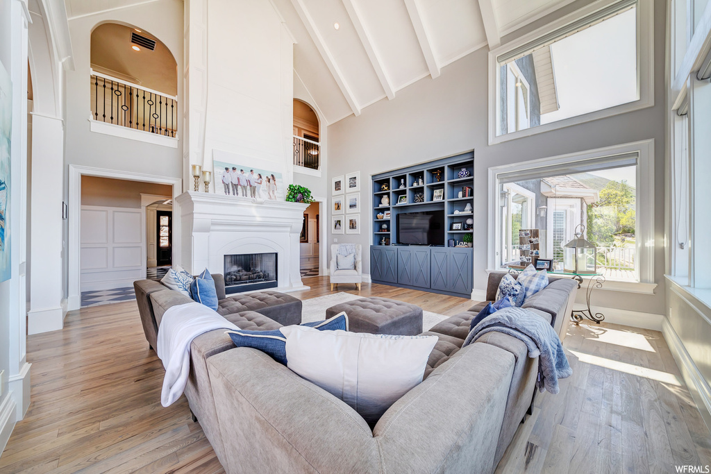 Hardwood floored living room with built in features, a fireplace, a high ceiling, and vaulted ceiling with beams