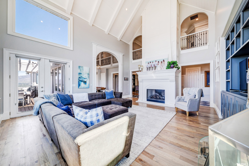Living room with built in features, a high ceiling, lofted ceiling with beams, light hardwood floors, and a fireplace