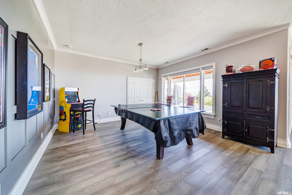 Game room with light hardwood flooring, ornamental molding, and a textured ceiling