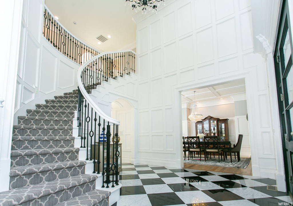Stairs featuring crown molding, a high ceiling, light tile flooring, a notable chandelier, and coffered ceiling
