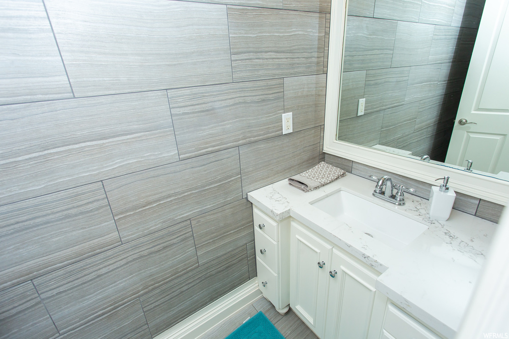 Bathroom featuring mirror, tile flooring, tile walls, and vanity