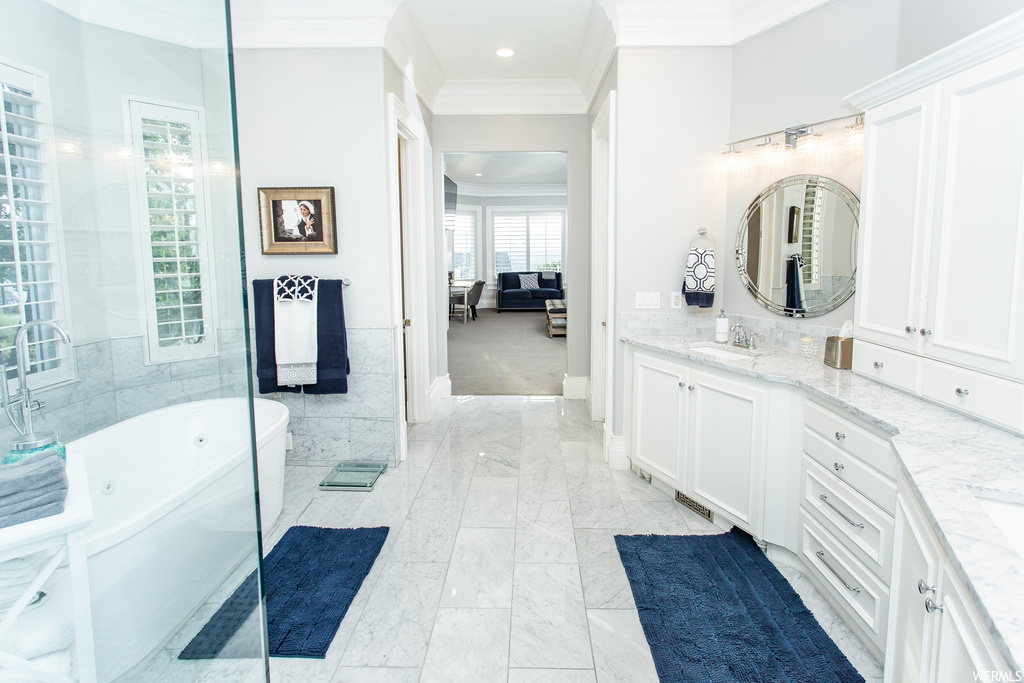 Bathroom featuring a washtub, ornamental molding, light tile flooring, mirror, and dual bowl vanity