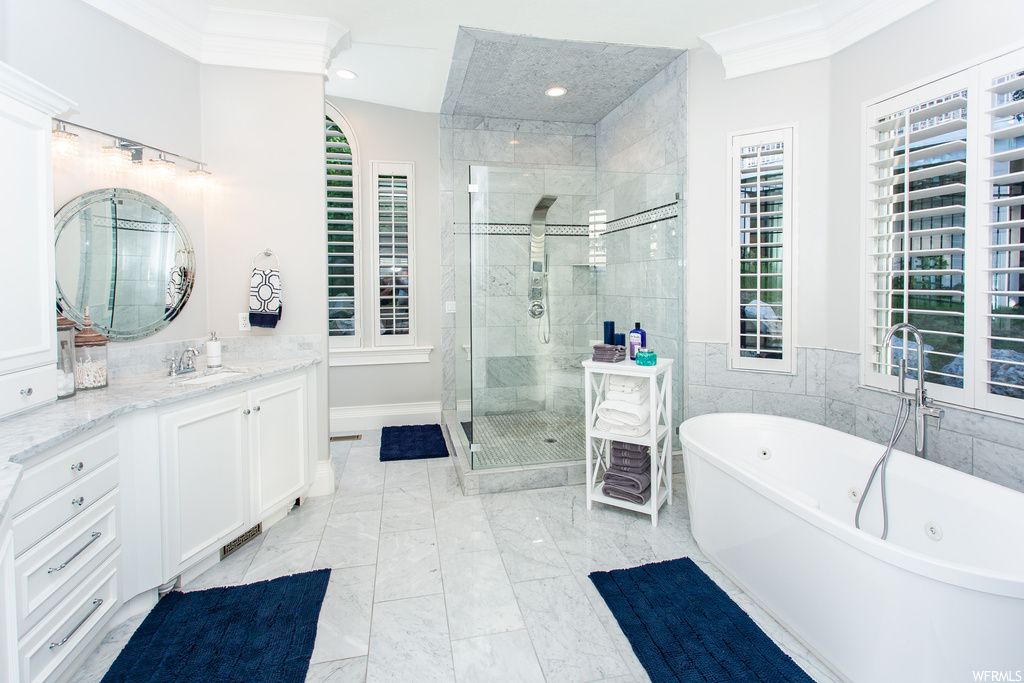 Bathroom with ornamental molding, mirror, vanity, light tile floors, and separate shower and tub