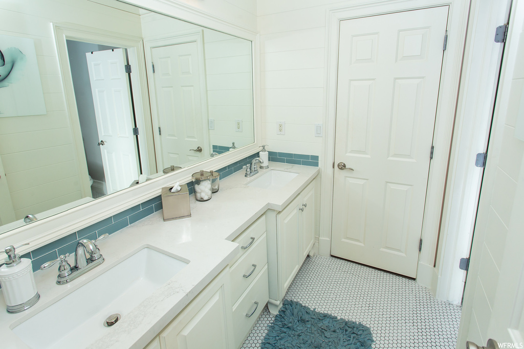 Bathroom with dual vanity, light tile floors, backsplash, and mirror