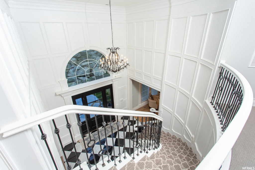 Stairway featuring a high ceiling, ornamental molding, and a notable chandelier