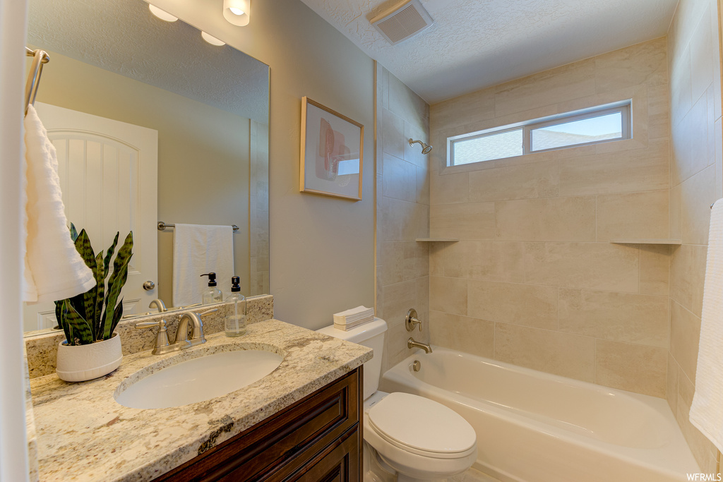 Full bathroom with vanity with extensive cabinet space, mirror, tiled shower / bath, and a textured ceiling