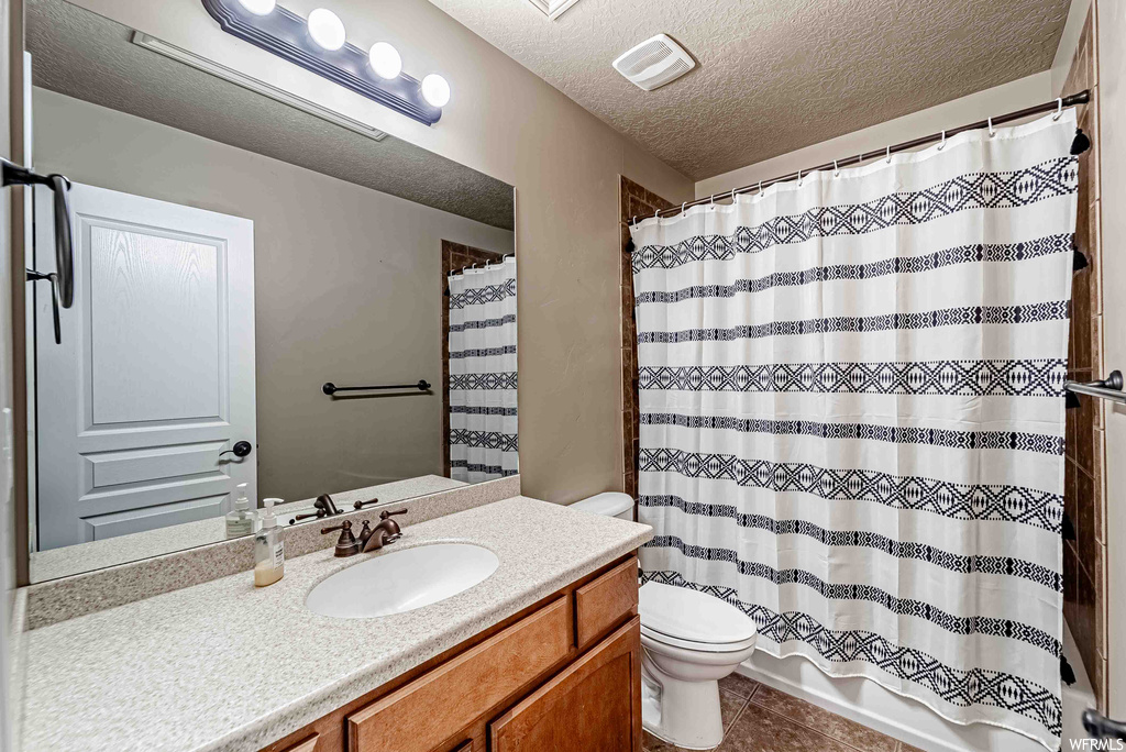 Bathroom with vanity with extensive cabinet space, tile flooring, mirror, and a textured ceiling