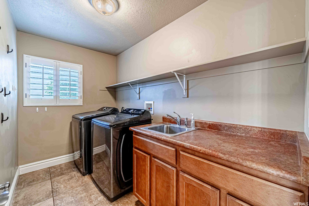Laundry room with separate washer and dryer, light tile flooring, and a textured ceiling