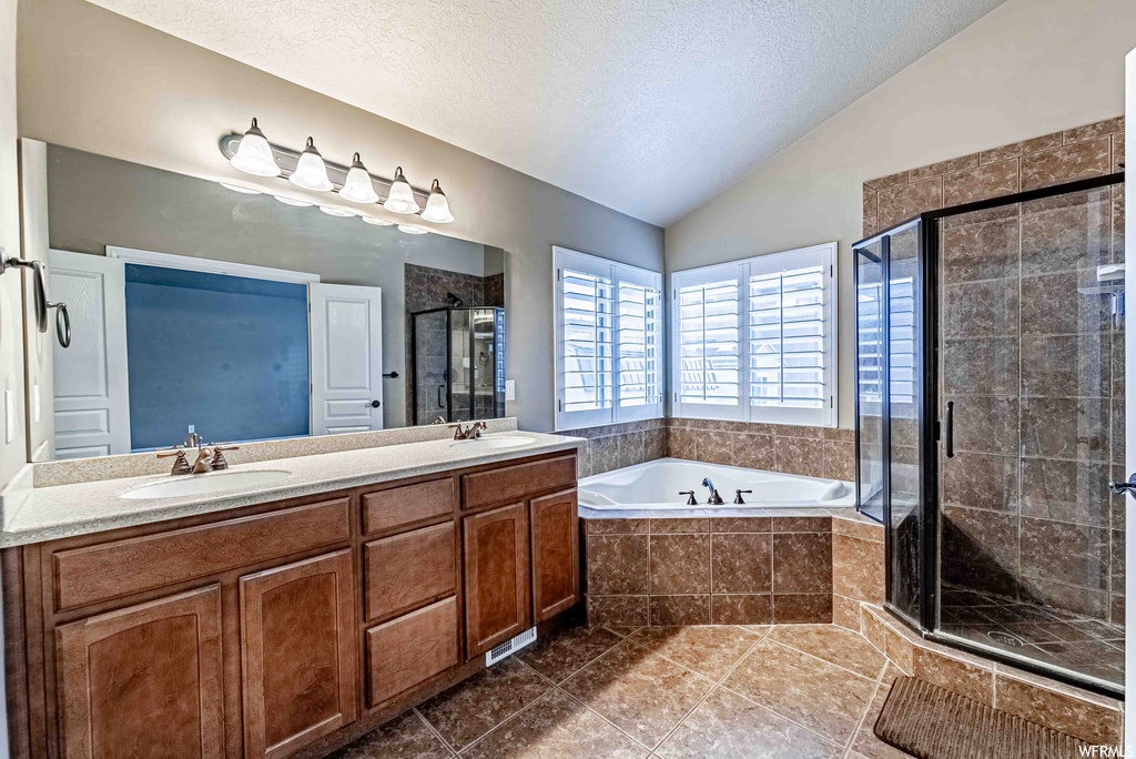 Bathroom with mirror, double large vanity, a textured ceiling, lofted ceiling, tile floors, and separate shower and tub