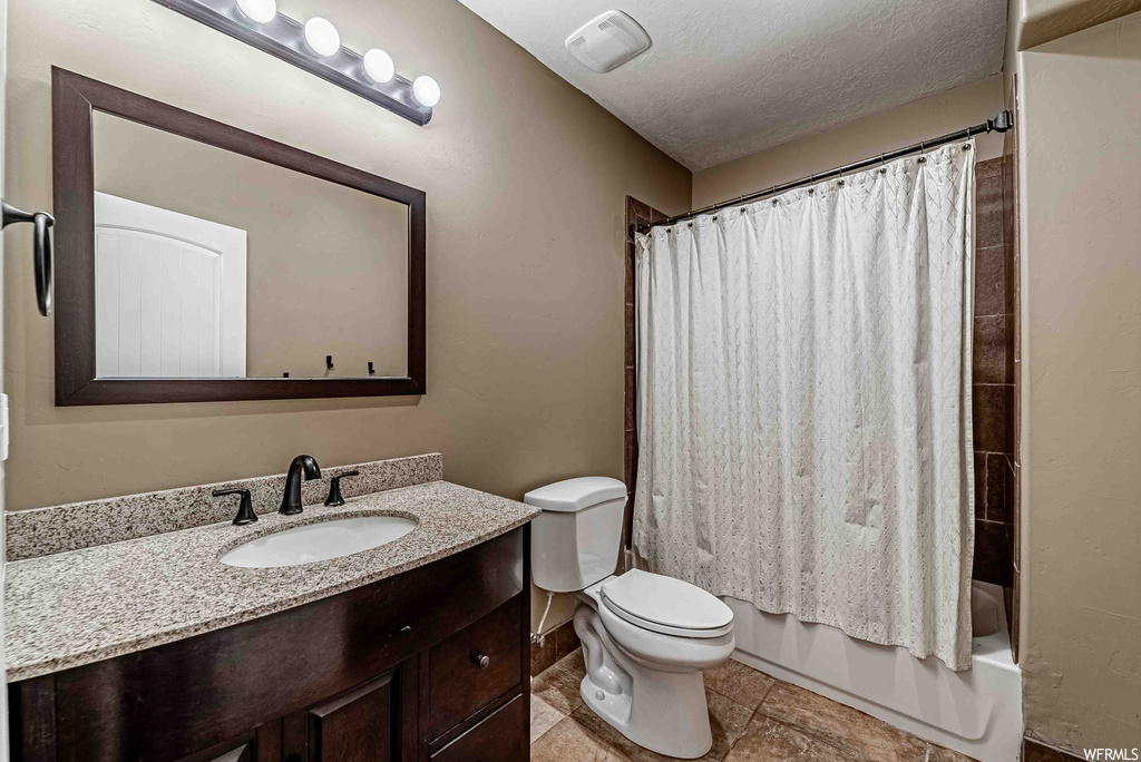 Full bathroom featuring mirror, a textured ceiling, oversized vanity, light tile floors, and shower / bath combo