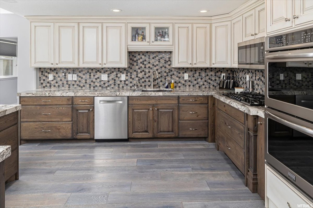 Kitchen featuring white cabinets, light hardwood flooring, stainless steel appliances, backsplash, and light countertops