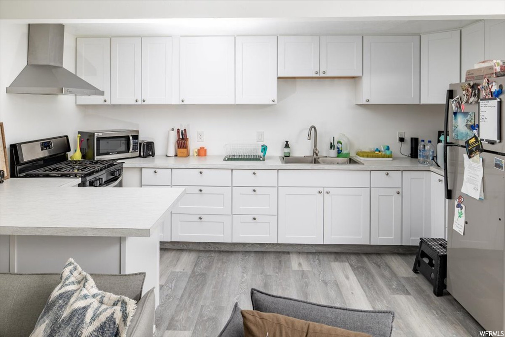 Kitchen featuring white cabinets, wall chimney exhaust hood, appliances with stainless steel finishes, light parquet floors, and light countertops