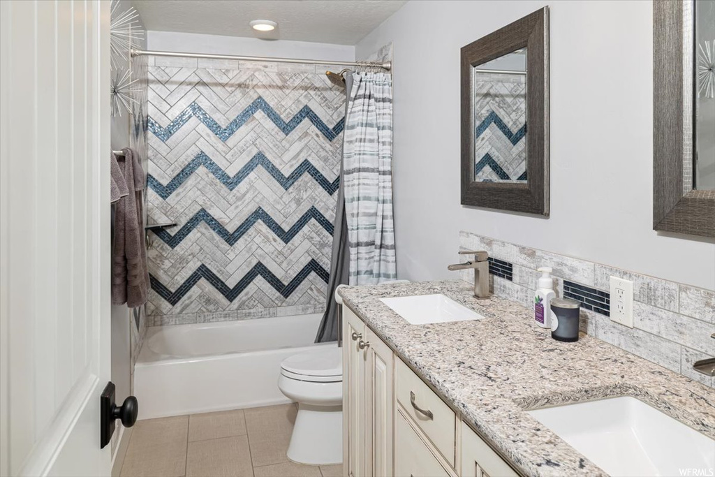 Full bathroom with shower / tub combo with curtain, mirror, light tile floors, and dual vanity
