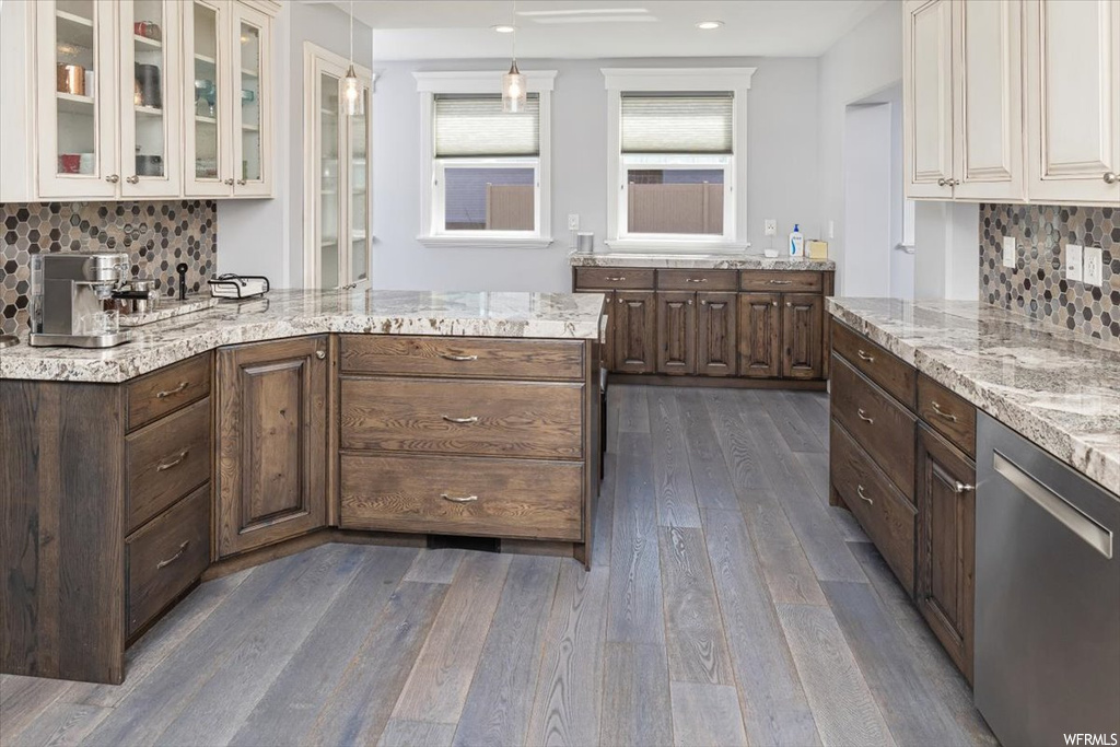 Kitchen with light hardwood flooring, stainless steel dishwasher, light granite-like countertops, and backsplash