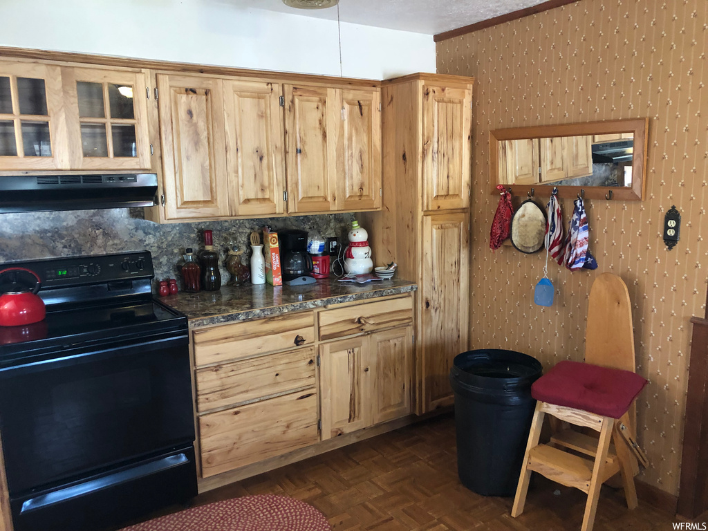 Kitchen with dark countertops, dark parquet flooring, range hood, backsplash, brown cabinets, and black range with electric stovetop