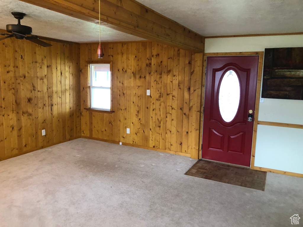 Foyer with wooden walls, beam ceiling, ceiling fan, and carpet floors