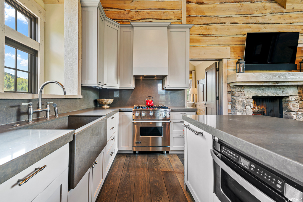Kitchen with dark hardwood floors, luxury range, wood walls, dishwashing machine, backsplash, and white cabinets