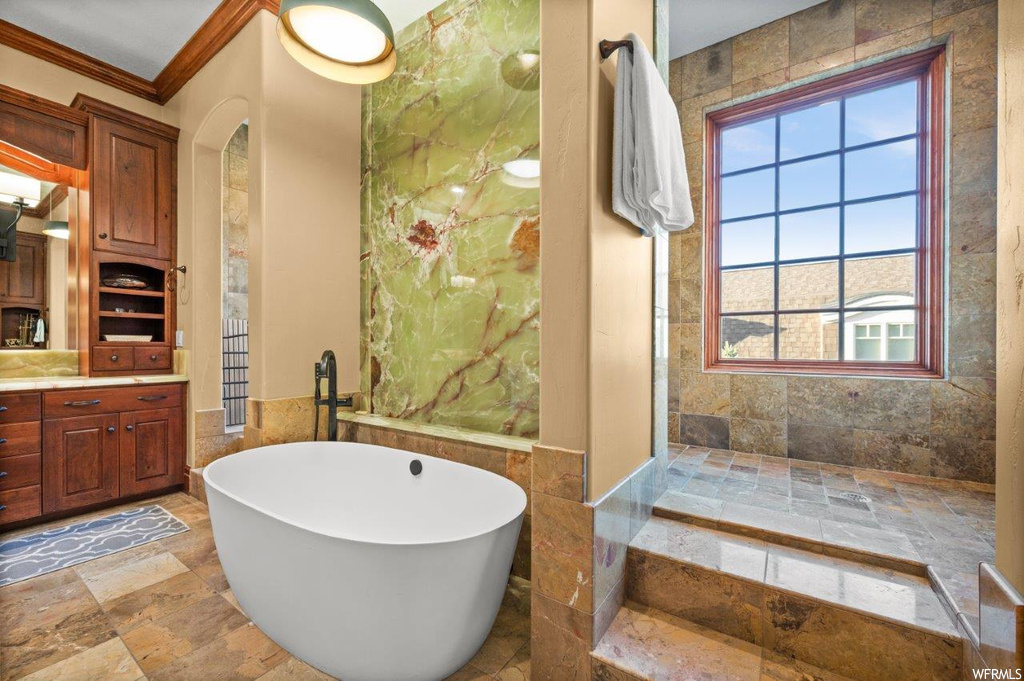 Bathroom with a tub, crown molding, tile walls, vanity, and light tile flooring