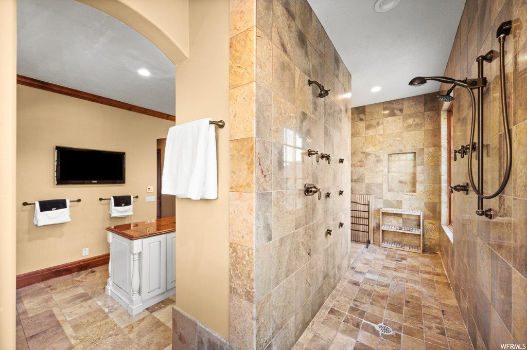 Bathroom featuring tiled shower, crown molding, vanity, and light tile floors