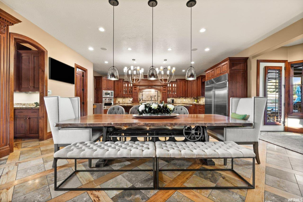 Kitchen with decorative light fixtures, a notable chandelier, dark brown cabinetry, backsplash, light tile flooring, light countertops, and built in appliances