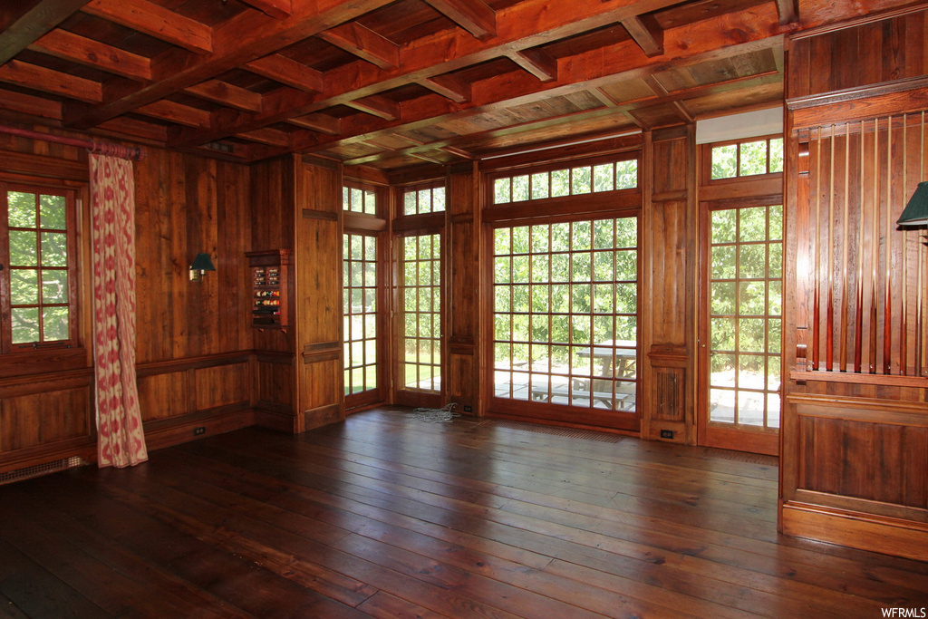 Empty room with beamed ceiling, wood ceiling, dark hardwood floors, wood walls, a healthy amount of sunlight, and coffered ceiling