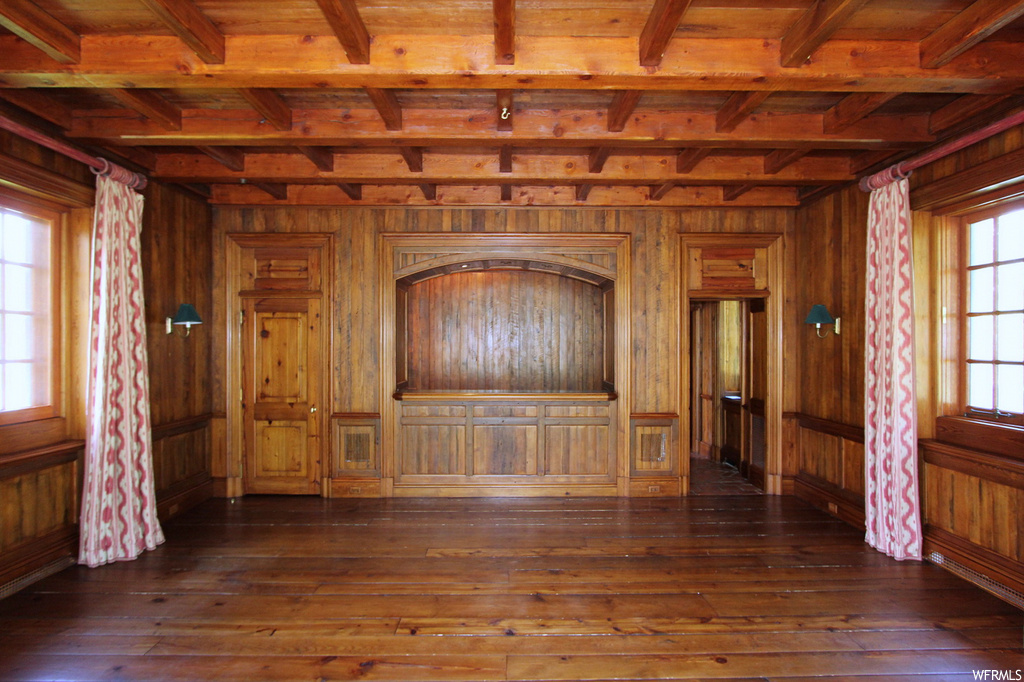 Empty room featuring beamed ceiling, wood walls, and dark hardwood floors
