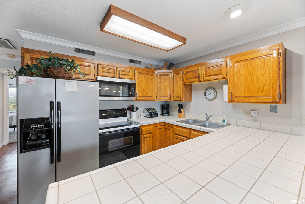 Kitchen with crown molding, stainless steel appliances, brown cabinets, light parquet floors, and light countertops