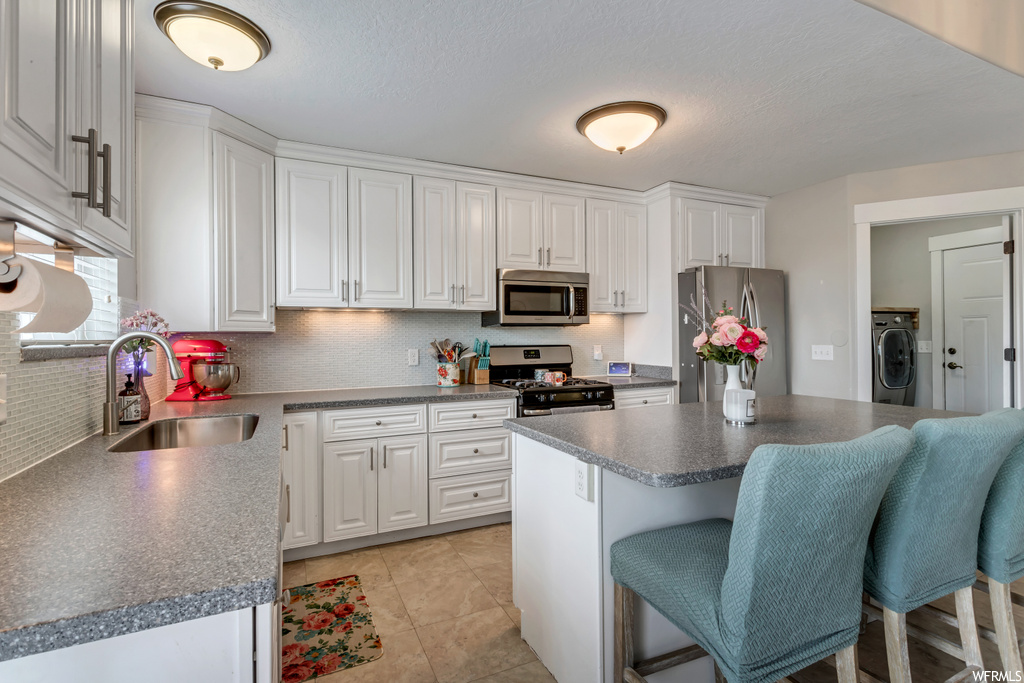 Kitchen with dark countertops, a center island, washer / dryer, stainless steel appliances, light tile floors, and white cabinetry