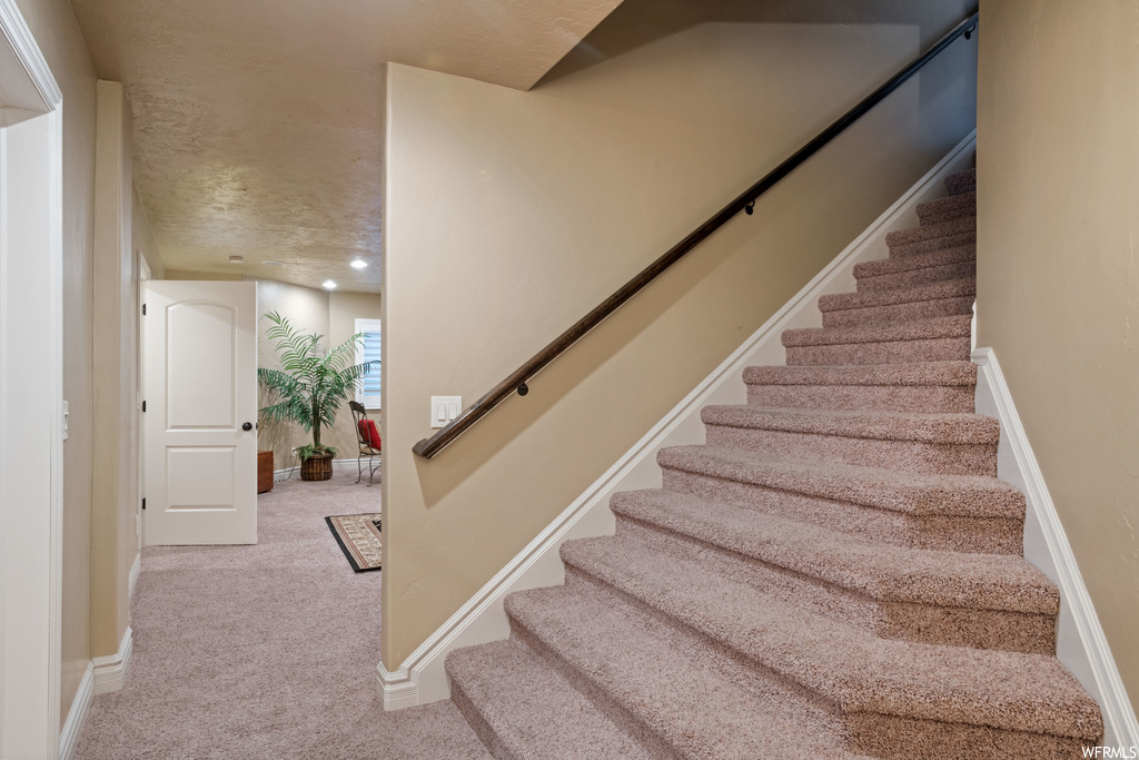 Stairs with light carpet and a textured ceiling