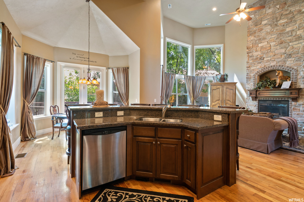 Kitchen featuring a fireplace, dark granite-like countertops, ceiling fan, light parquet floors, and stainless steel dishwasher