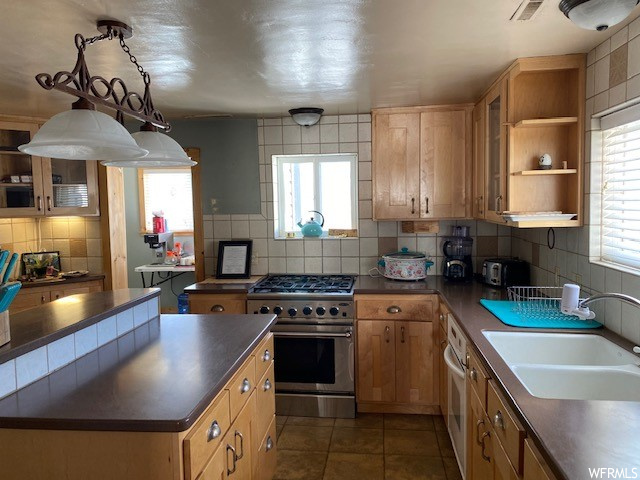 Kitchen featuring brown cabinets, dark tile floors, dark countertops, backsplash, and high end stainless steel range oven