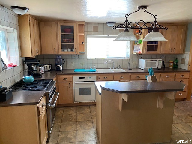 Kitchen featuring brown cabinets, white appliances, tile flooring, dark countertops, and backsplash