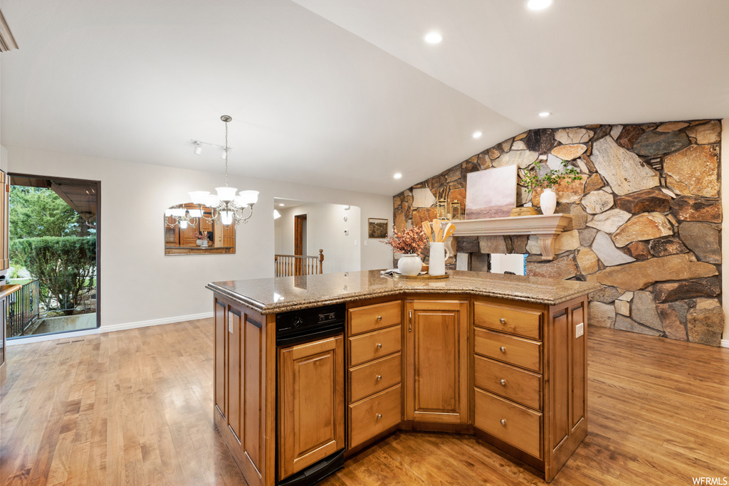 Kitchen featuring light stone countertops, brown cabinets, light hardwood floors, and lofted ceiling