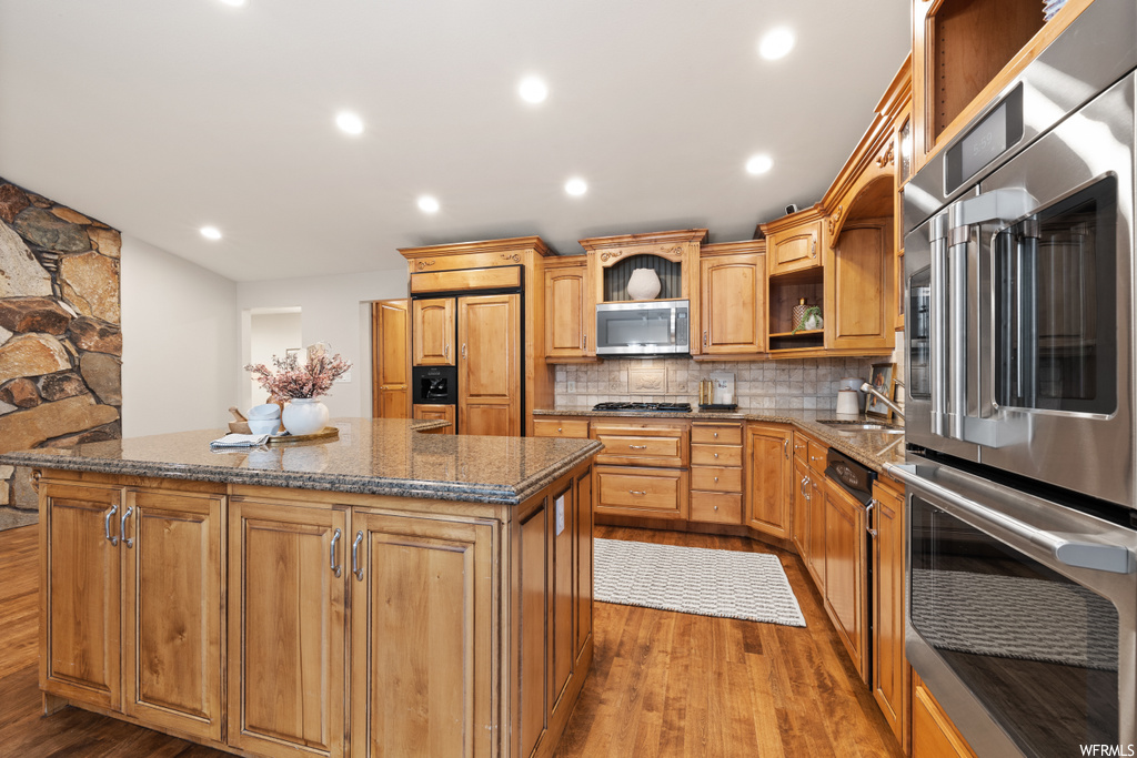 Kitchen with backsplash, brown cabinets, dark stone countertops, and light hardwood floors
