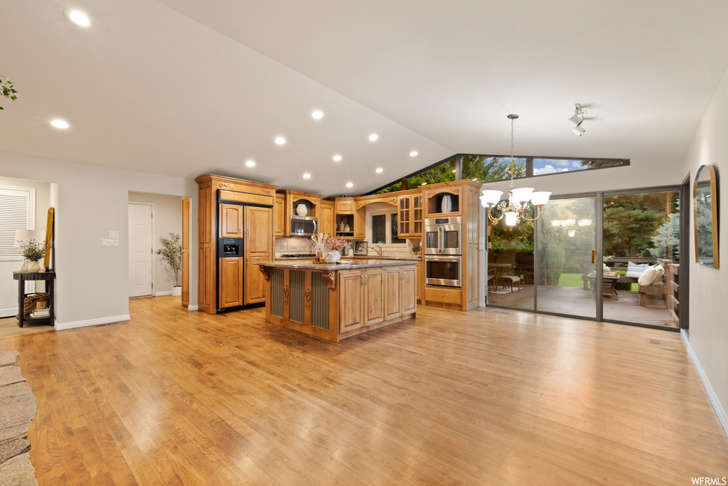 Kitchen with appliances with stainless steel finishes, lofted ceiling, light hardwood flooring, a center island with sink, backsplash, and a high ceiling