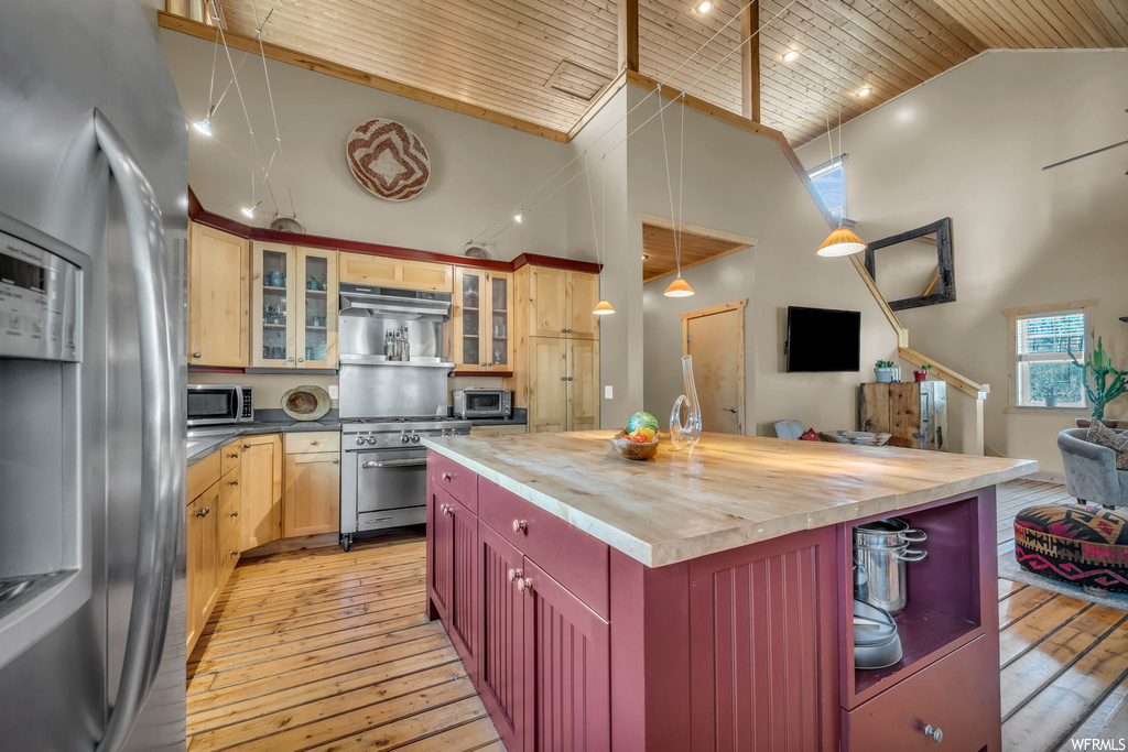 Kitchen featuring light countertops, light hardwood floors, wooden ceiling, appliances with stainless steel finishes, lofted ceiling, pendant lighting, a kitchen island with sink, and a high ceiling