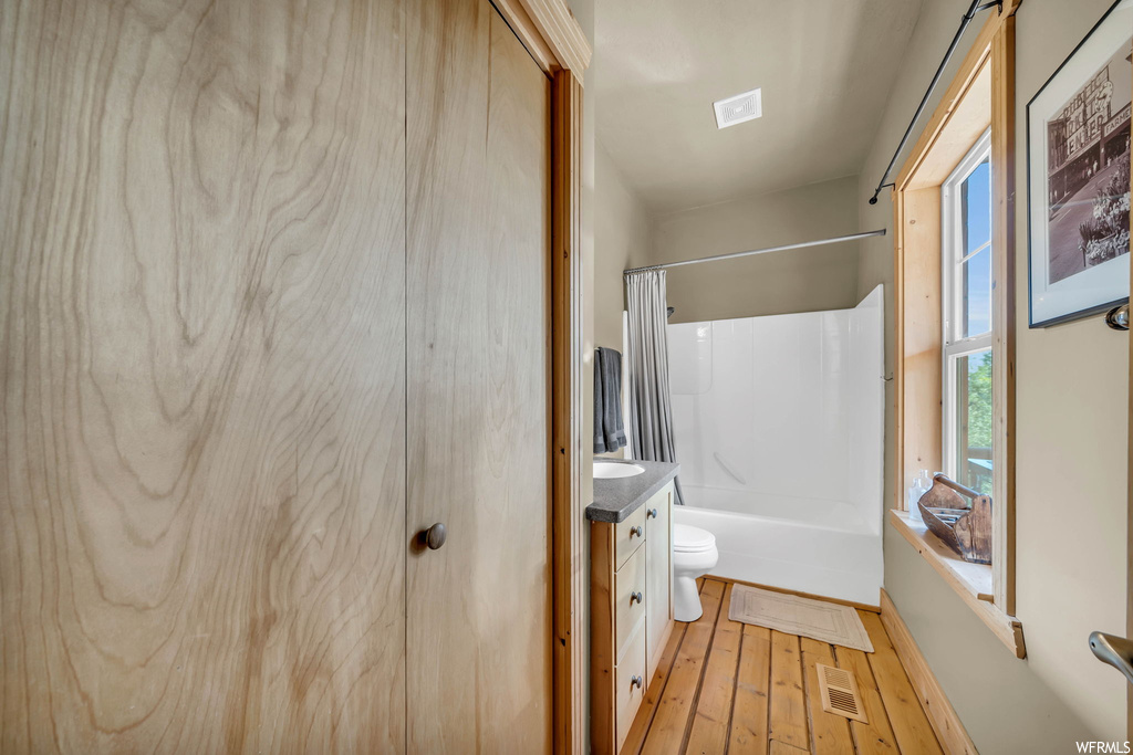 Full bathroom featuring light hardwood flooring, vanity, and shower / bath combination with curtain