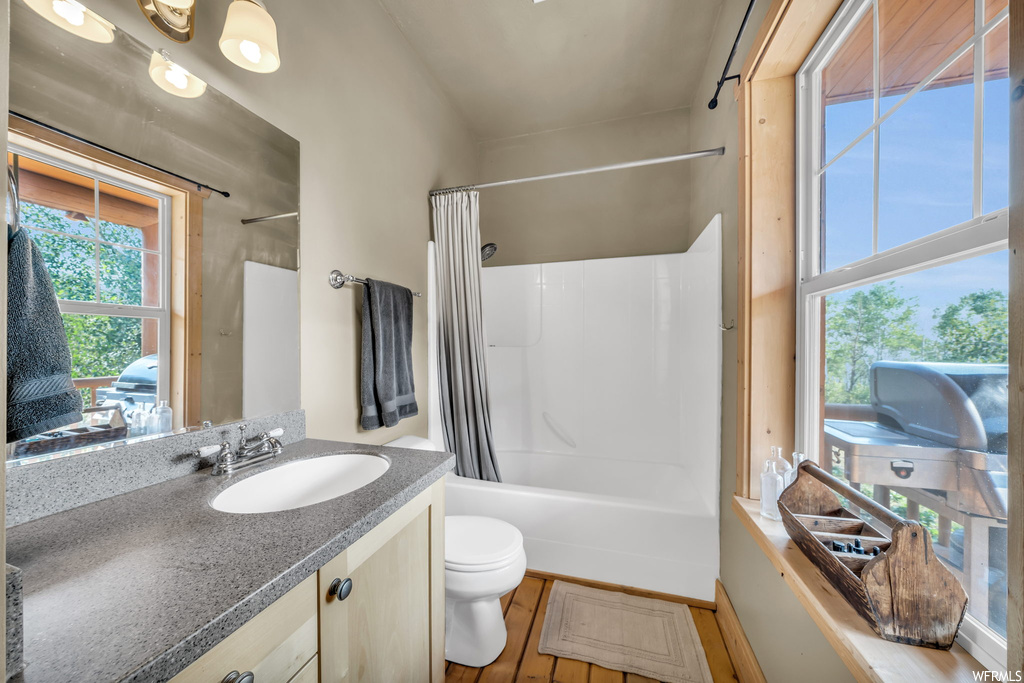 Full bathroom with vanity with extensive cabinet space, shower / bath combination with curtain, mirror, and light hardwood floors