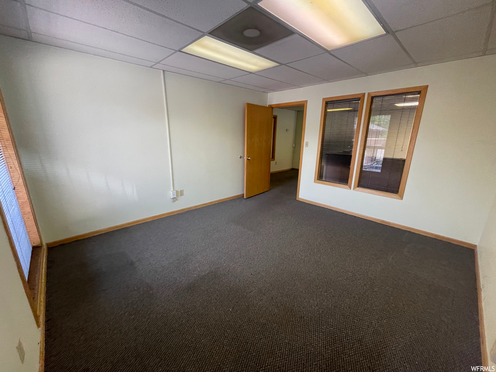 Unfurnished room featuring dark carpet and a drop ceiling